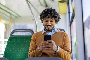 Young man sitting on bus using smartphone, smiling and engaged in digital content. Casual attire and relaxed atmosphere emphasize modern urban lifestyle and connectivity during commute. photo