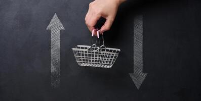 Concept of economic fluctuations and consumer behavior, featuring a hand holding a small shopping basket suspended between two arrows pointing up and down. photo