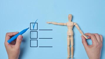 Concept of making decisions and completing tasks, wooden dummy in hand, other hand marking a checkbox on a list. Symbolizes control, choosing and completing tasks, decision making photo