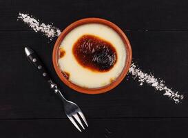 Turkish rice pudding sutlac serving in earthenware bowl on black rustic table photo