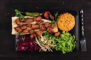 Turkish cuisine - traditional shish kebab with bulgur and vegetables on a black plate photo