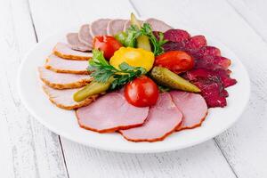 Plate combining several types of meat cuts and pickles being served on white table photo
