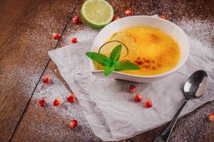 Delicious creme brulee decorated with lime and mint on wooden table photo