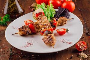 Grilled chicken and bell pepper skewers with cherry tomatoes and spices on a white plate photo