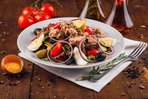 Fresh nicoise salad with tuna on a wooden table being prepared with eggs and tomatoes around photo