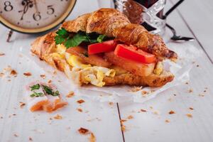 Delicious croissant filled with ham, scrambled eggs and tomato for breakfast photo