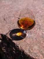 Glass of cognac standing on a rock in the sunlight photo
