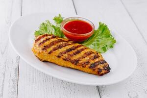 Grilled chicken breast served with lettuce and sauce on white plate photo