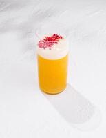 Refreshing yellow cocktail with white foam and raspberry powder topping on white background photo