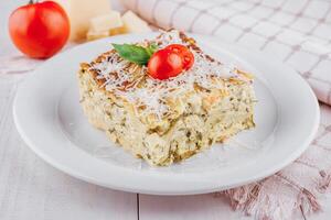 Slice of vegetarian lasagna garnished with fresh ingredients on white plate photo