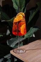Refreshing aperol spritz cocktail standing on a table with tropical plants in the background photo