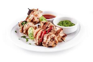 Grilled chicken skewers with vegetables and dipping sauces on white plate photo