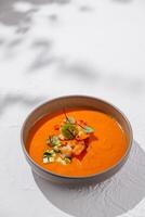 Bowl of gazpacho soup with shrimp and cucumber toppings standing on white table photo
