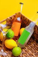Bottles of refreshing summer drinks with limes and lemons in wicker basket photo