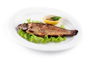 Grilled trout served on bed of lettuce with lemon and condiment photo