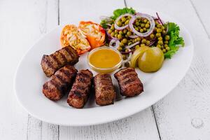 Grilled minced meat kebab with mustard, pickles, and green pea salad on white plate photo