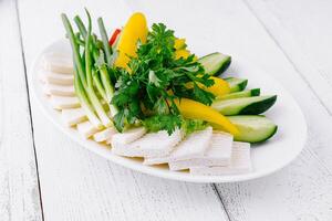 White plate showing sliced cheese with cucumber and green onions on white table photo