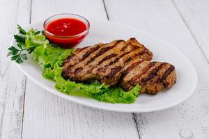 Grilled steak lying on fresh lettuce with tomato sauce on white plate photo