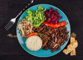 Delicious iskender kebab is served on a blue plate with rice, fresh vegetables and pita bread photo
