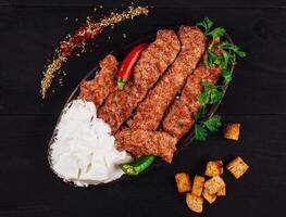 Spicy lule kebab served on a traditional plate with yogurt and croutons photo