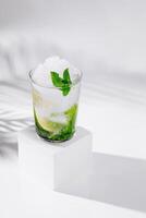 Refreshing mojito cocktail standing on white cube with tropical palm leaf shadow photo