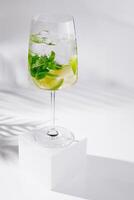 Refreshing summer cocktail with lime and mint standing on white cube photo