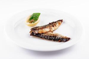 Grilled mackerel fillets served on white plate with lemon and basil garnish photo