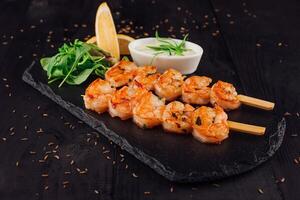 Grilled tiger prawns skewers served on stone plate with herbs and lemon photo