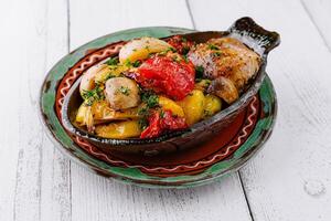 Delicious roasted vegetables and chicken breast served in rustic clay pot photo