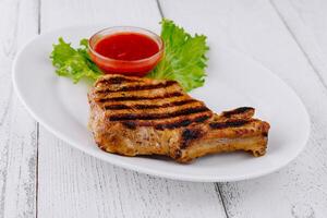 Grilled pork chop resting on white plate with lettuce and tomato sauce photo