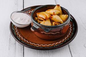 Small baked pies are lying in a ceramic bowl on a white wooden table photo