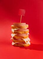 Big tower made of bread, sausage and cheese with blank red flag on the top standing on red background photo