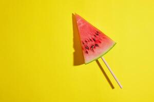 triangular piece of watermelon on a stick on a yellow background photo