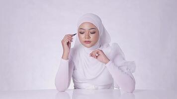 Young girl asia in hijab charming look at camera hand holding eyebrow pencil and cap with clean healthy shiny skin isolated on white background video