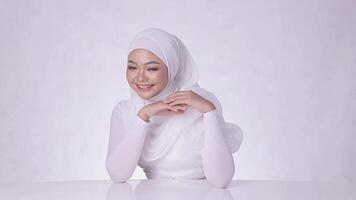 The charm of a cheerful veiled girl with perfect and healthy radiant white skin, hands on the table and left arm isolated on a white background video