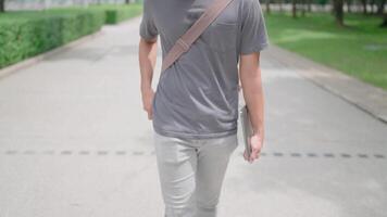Asian man walking with laptop and bag in the park, phone call comes in, picks up phone, answers call and talks, walking, studying, he is walking in nature to relax from work and study, studying online video