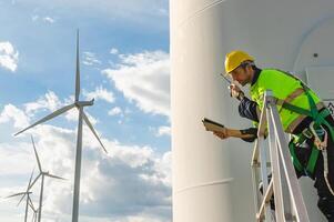 man in a yellow helmet is standing on a ladder next to a wind turbine photo