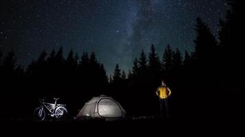 Tourist near tent in night forest. The Milky Way moves in the night sky. Timelapse. Travel concept. 4K video