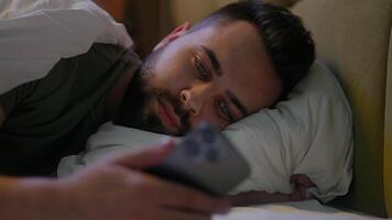 Caucasian man lying in bed bedroom user mobile phone smartphone cellphone gadget technology male guy connected scrolling website browsing network cyber ecommerce chatting internet distance communicate video