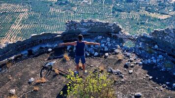 Tourist standing with open arms on ancient ruins overlooking olive tree field photo