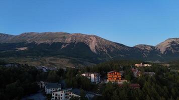 Golden hues of dusk illuminate a serene hillside village nestled beneath majestic mountains in tranquil evening light photo
