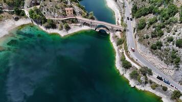 Aerial view of a serene lake bordered by rocky hills and a charming bridge during a sunny day in nature photo