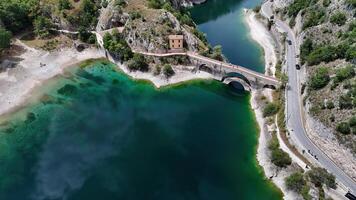 A serene aerial view of a picturesque bridge over turquoise waters near a charming abandoned building surrounded by rocky landscape photo