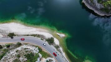 A serene winding road curves along a tranquil turquoise lake surrounded by lush greenery on a sunny day photo