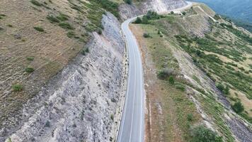 Winding mountain road surrounded by rugged terrain in a serene landscape during the afternoon sunlight photo
