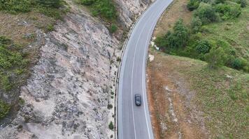 A solitary car navigates the winding road beside a rocky cliff in a scenic landscape on a calm, cloudy day photo
