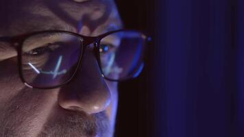 Close-up of a doctor in glasses intensely working on a computer. Reflections of heart cardiogram and analytics in the glasses highlight expertise in cybersecurity and software development. video