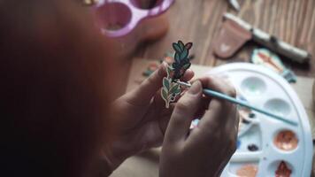 Girl paints black acrylic color pin with image of branch with berries and flowers. Process of decorating brooch made of plywood with pattern applied by laser machine. Handmade and diy in workshop. video