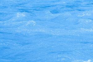 Bluewater waves on the surface ripples blurred. Defocus blurred transparent blue colored clear calm water surface texture with splash and bubbles. Water waves with shining pattern texture background. photo