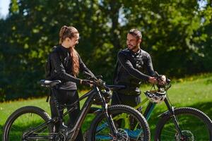 A sweet couple, equipped with bicycles and engrossed in coordinating their journey, checks their GPS mobile and watches while planning scenic routes in the park, seamlessly blending technology and photo
